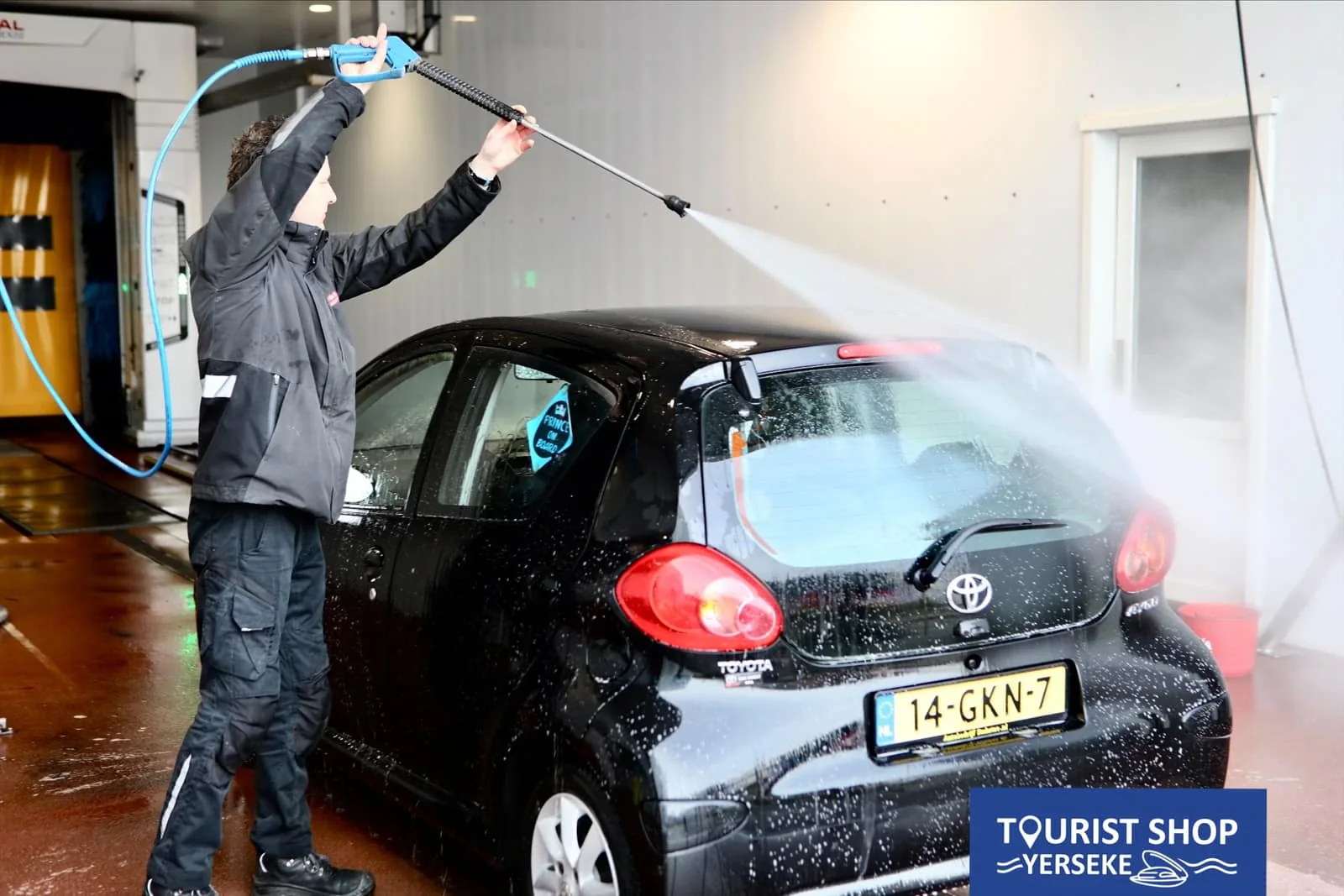 Man spuit een zwarte auto af met de hogedrukspuit