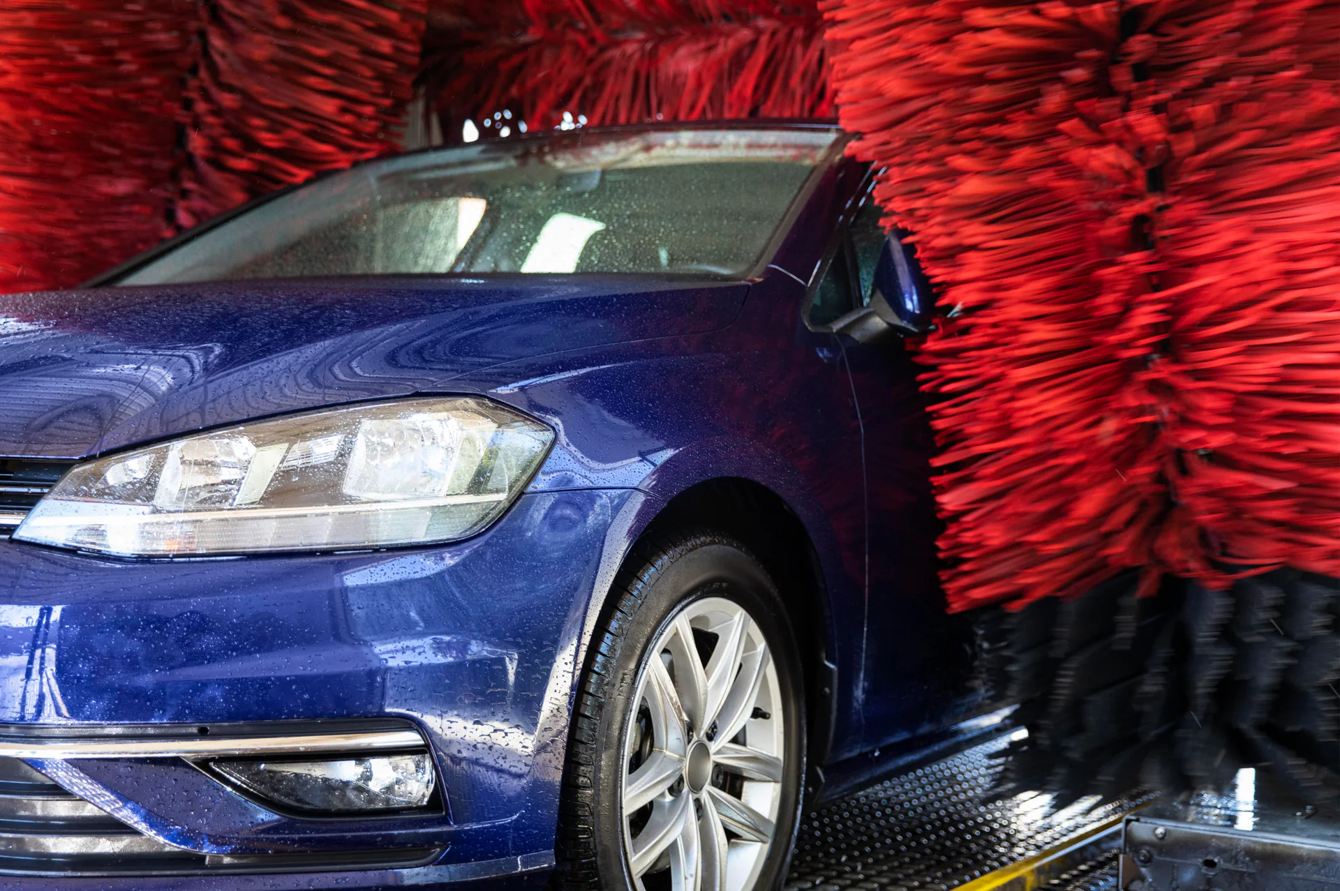 Blauwe auto tussen rode borstels in een wasstraat