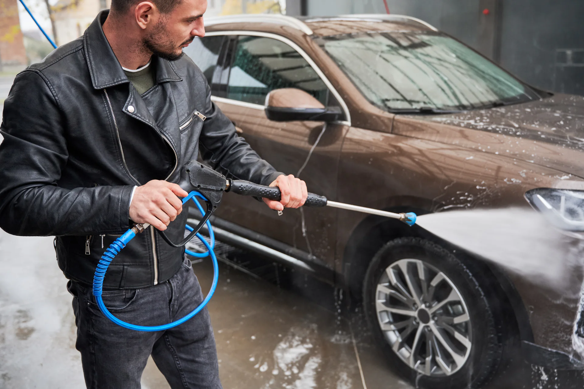 Man spuit in een wasbox de velg van een bruine auto af met de hogedrukspuit