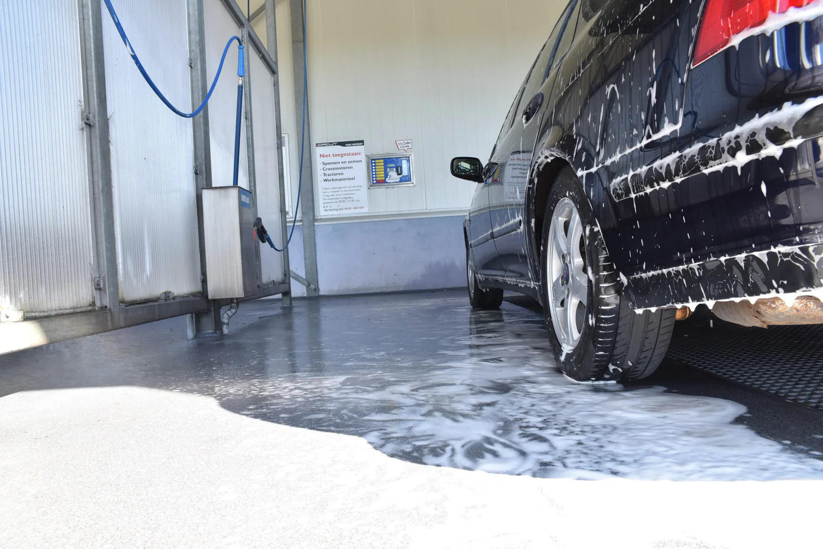 Auto met schuim in een wasbox met blauwe hogedrukslang – Van Hemert Carwash Zaltbommel, Zaltbommel
