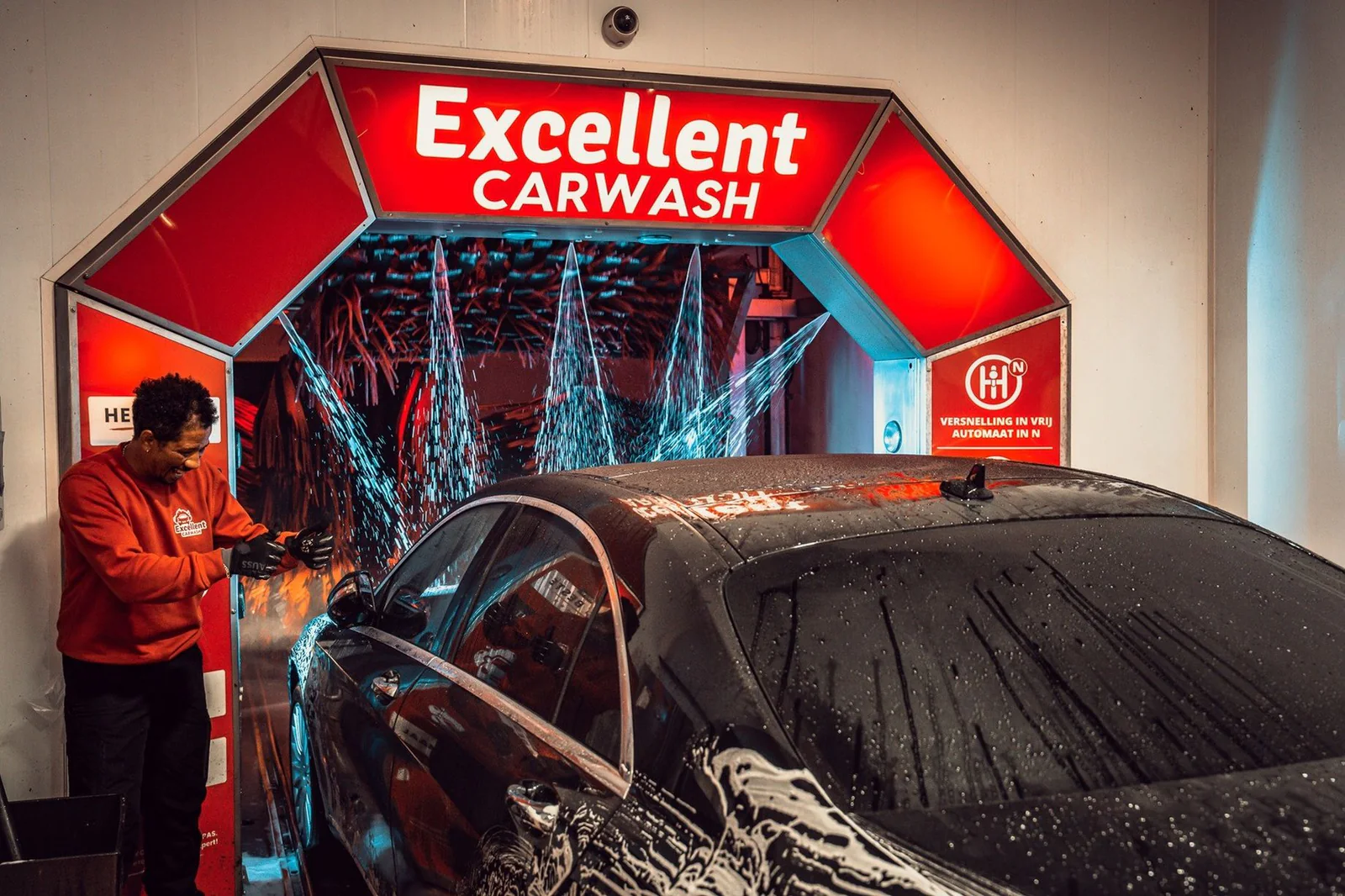 Medewerker bij de voorwas onder de rode Excellent Carwash-boog – Excellent Carwash Amsterdam, Amsterdam