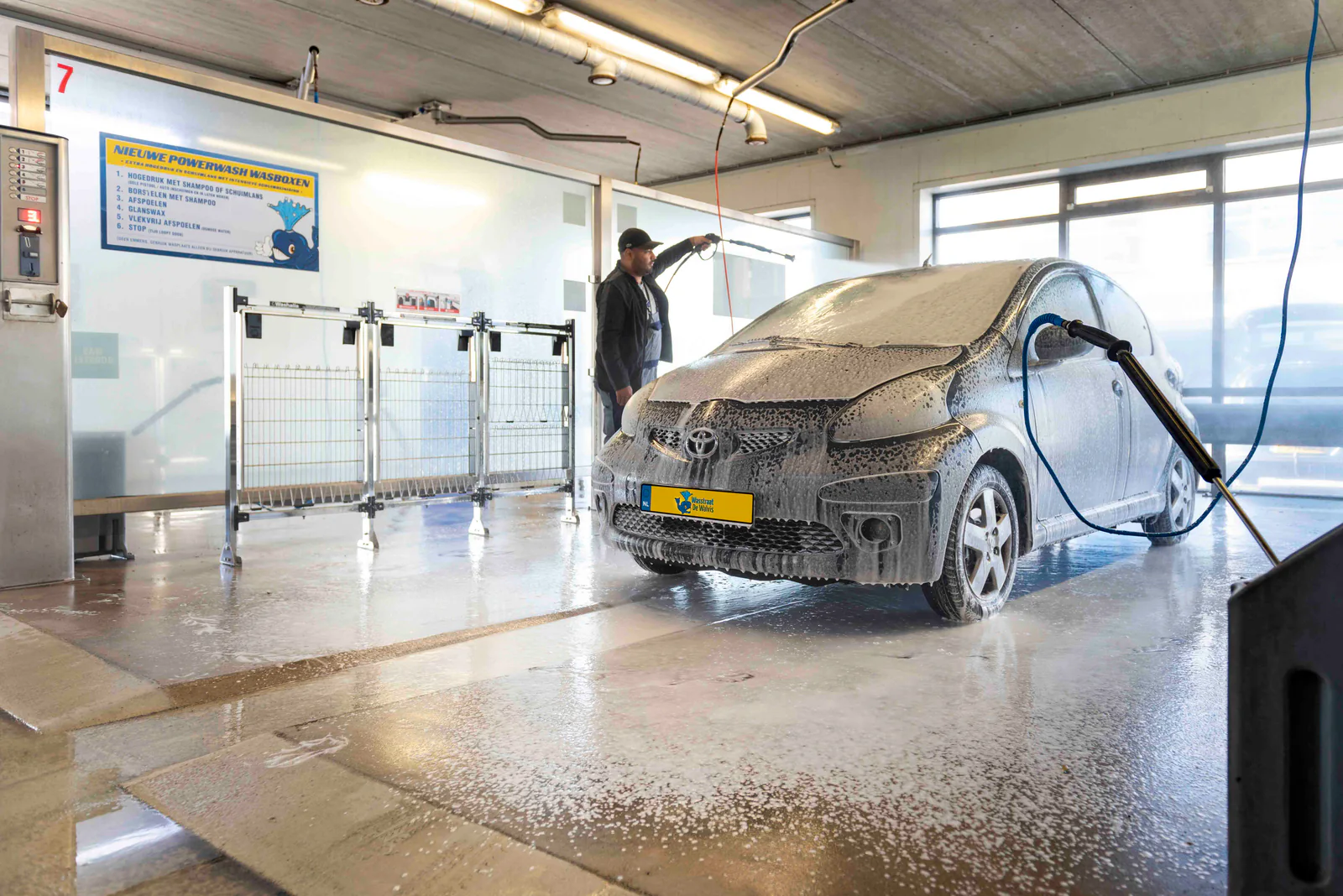 Man spuit een auto onder het schuim af met de hogedrukspuit in een overdekte wasbox